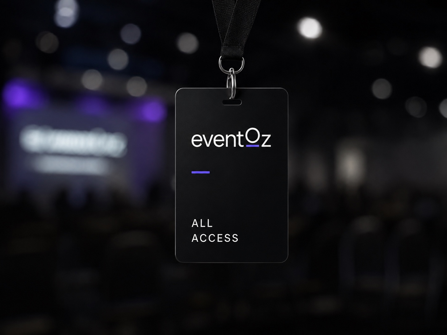 eventOz all-access badge on a lanyard, in front of a darkened conference hall with stage lighting